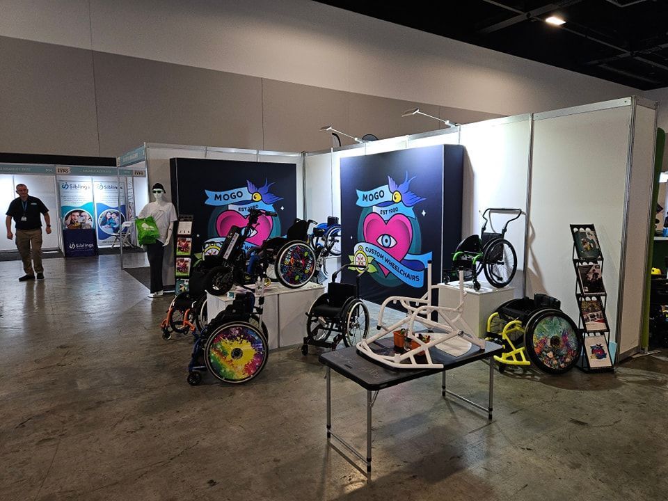 Wheelchair display at a conference. Various chairs are shown against a backdrop with a heart logo.
