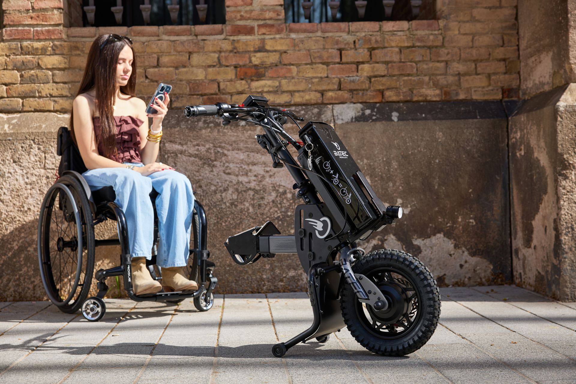 Woman in a wheelchair looking at a black motorized mobility device on a sidewalk.