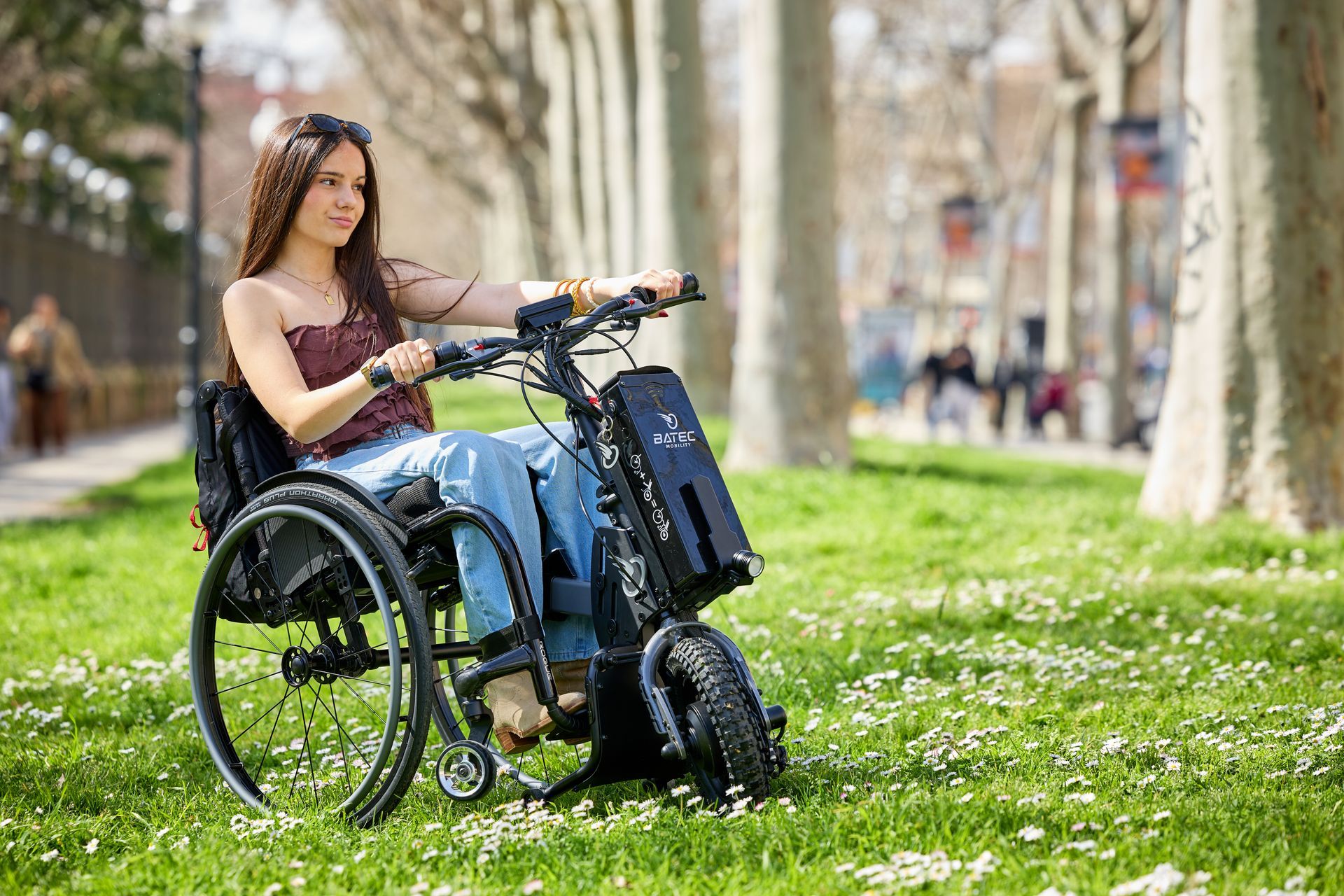 Woman in a wheelchair using a smartphone in a grassy park path