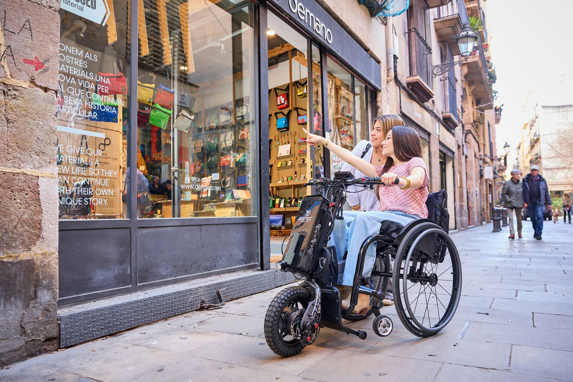 Person in wheelchair pointing at a shop window on a narrow city street