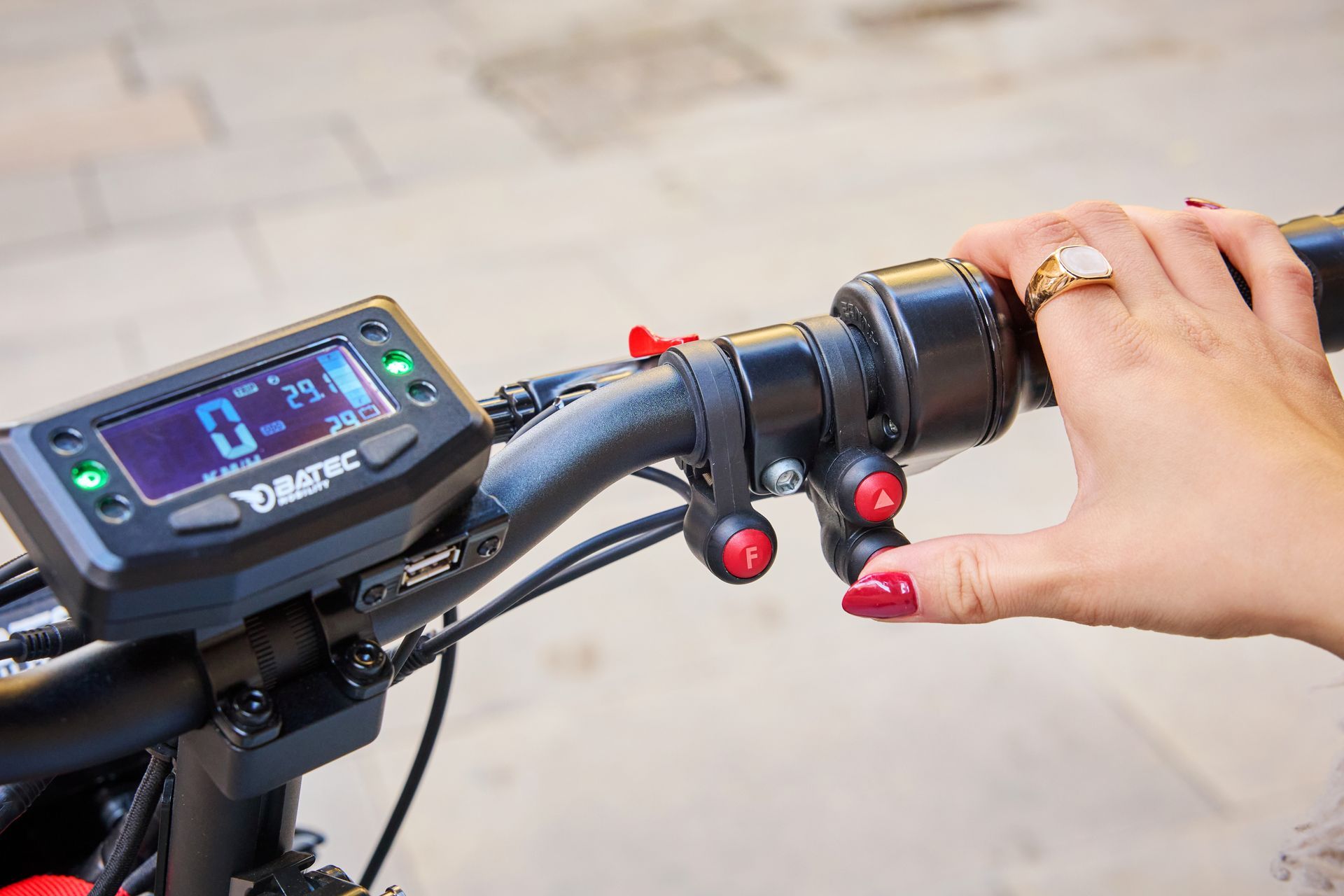 Hand on electric bike handlebar with digital display and control buttons on paved path