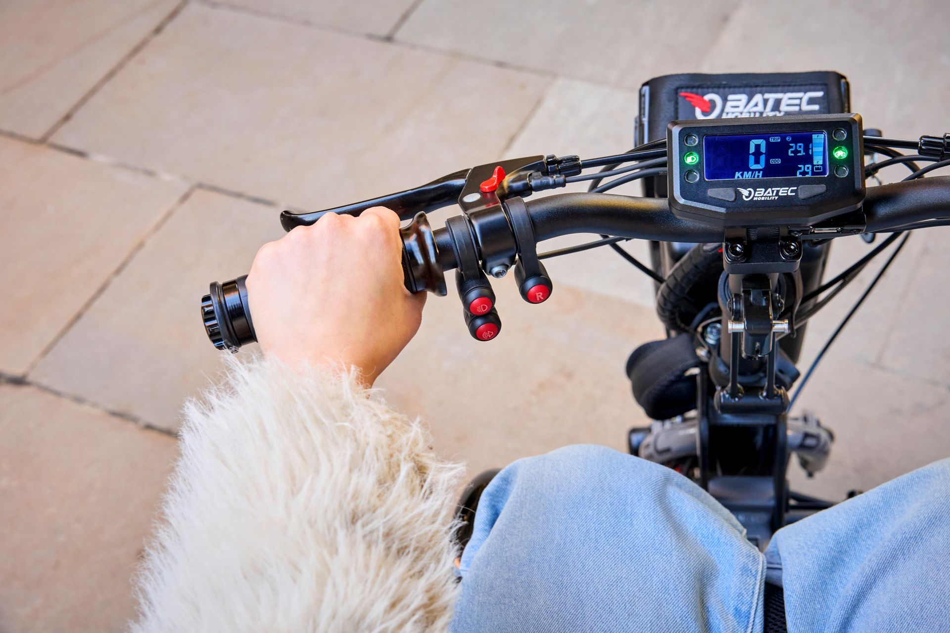Close-up of a rider’s hands on an electric bike handlebar with a digital display and red levers
