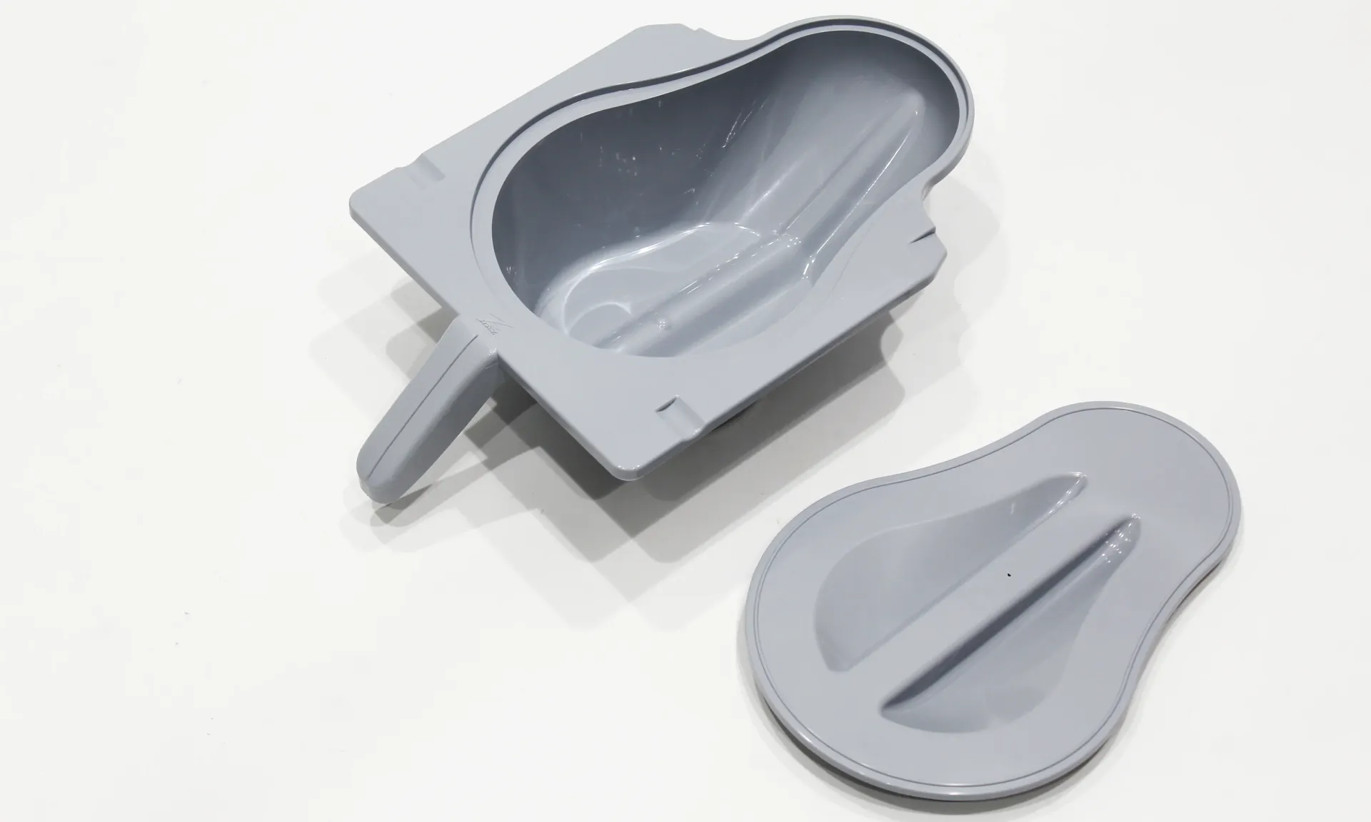 Gray plastic bedpan with a detached lid on a white surface.