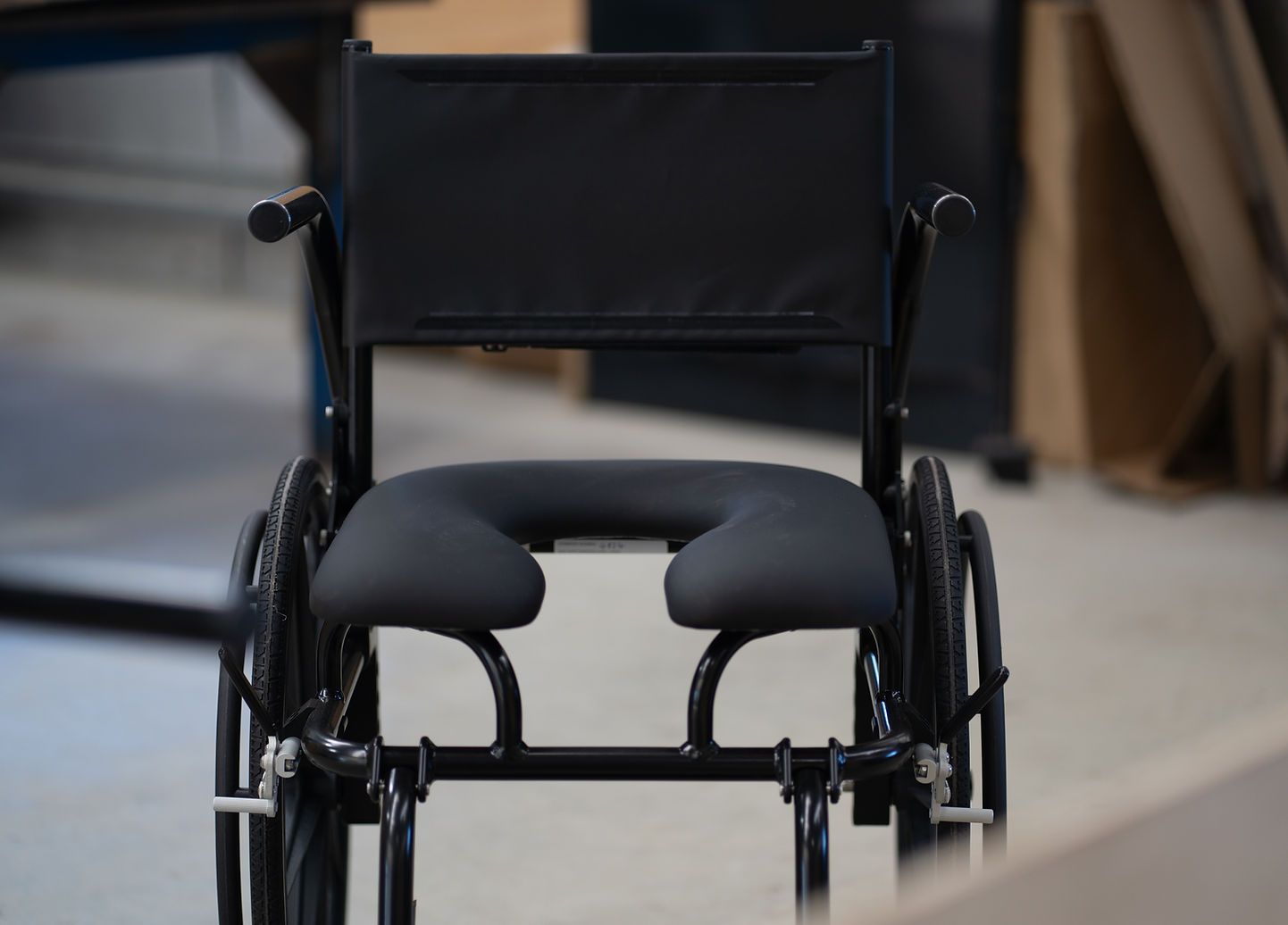 Black shower chair with a U-shaped seat, armrests, footrest, and wheels.
