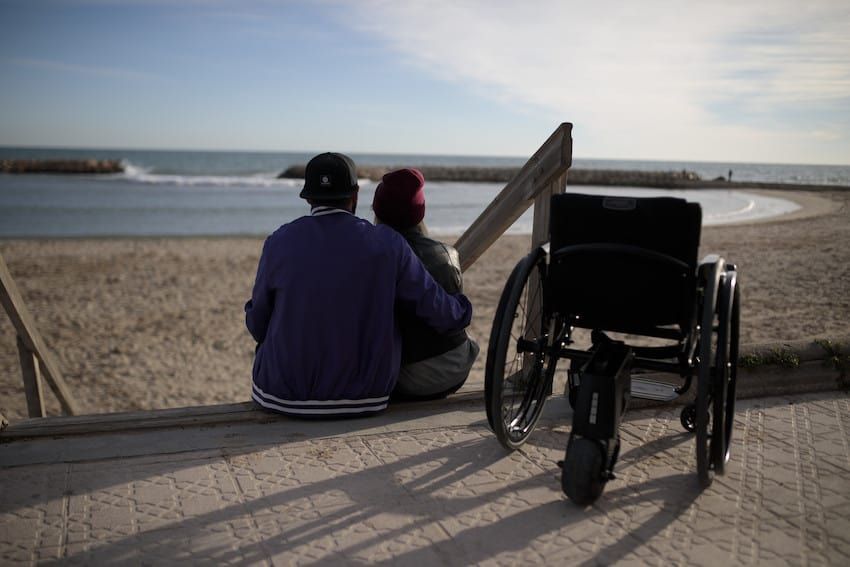 Wheelchair with a black seat and a black storage bag. The wheels are silver with green accents.