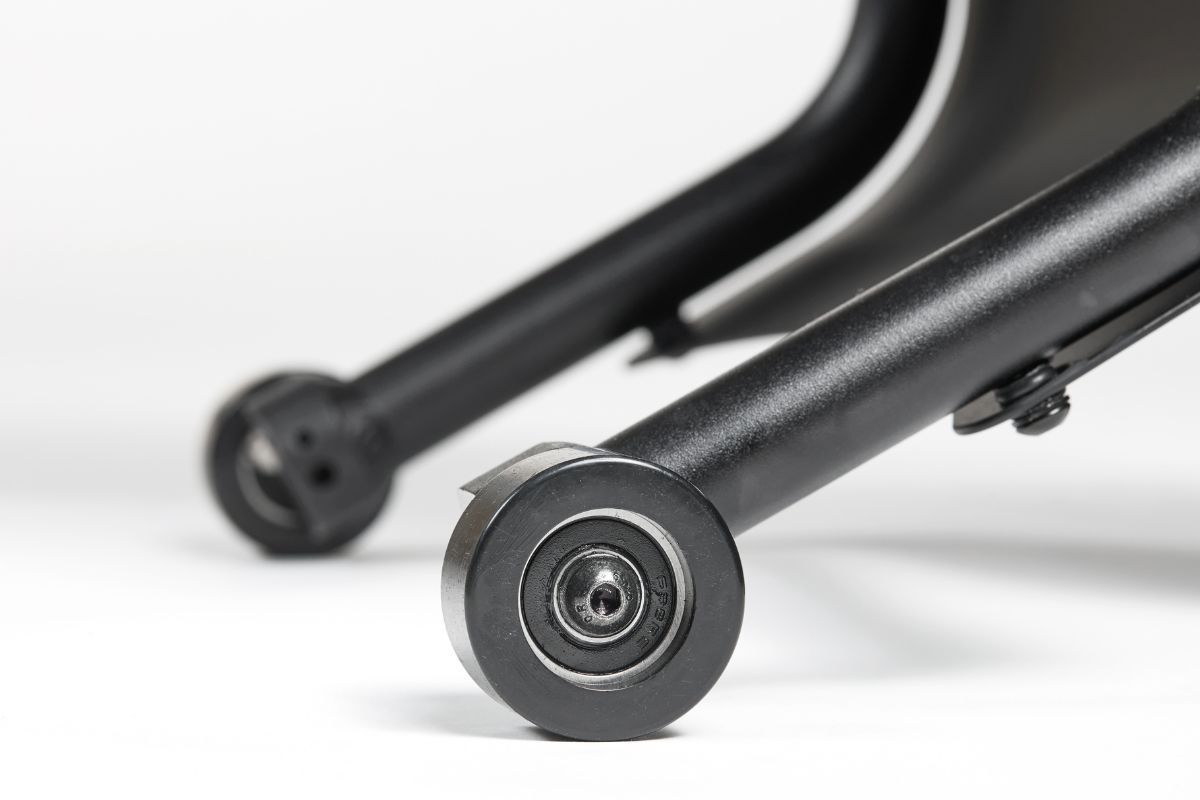 Close-up of black metal frame with two small, cylindrical wheels. White background.