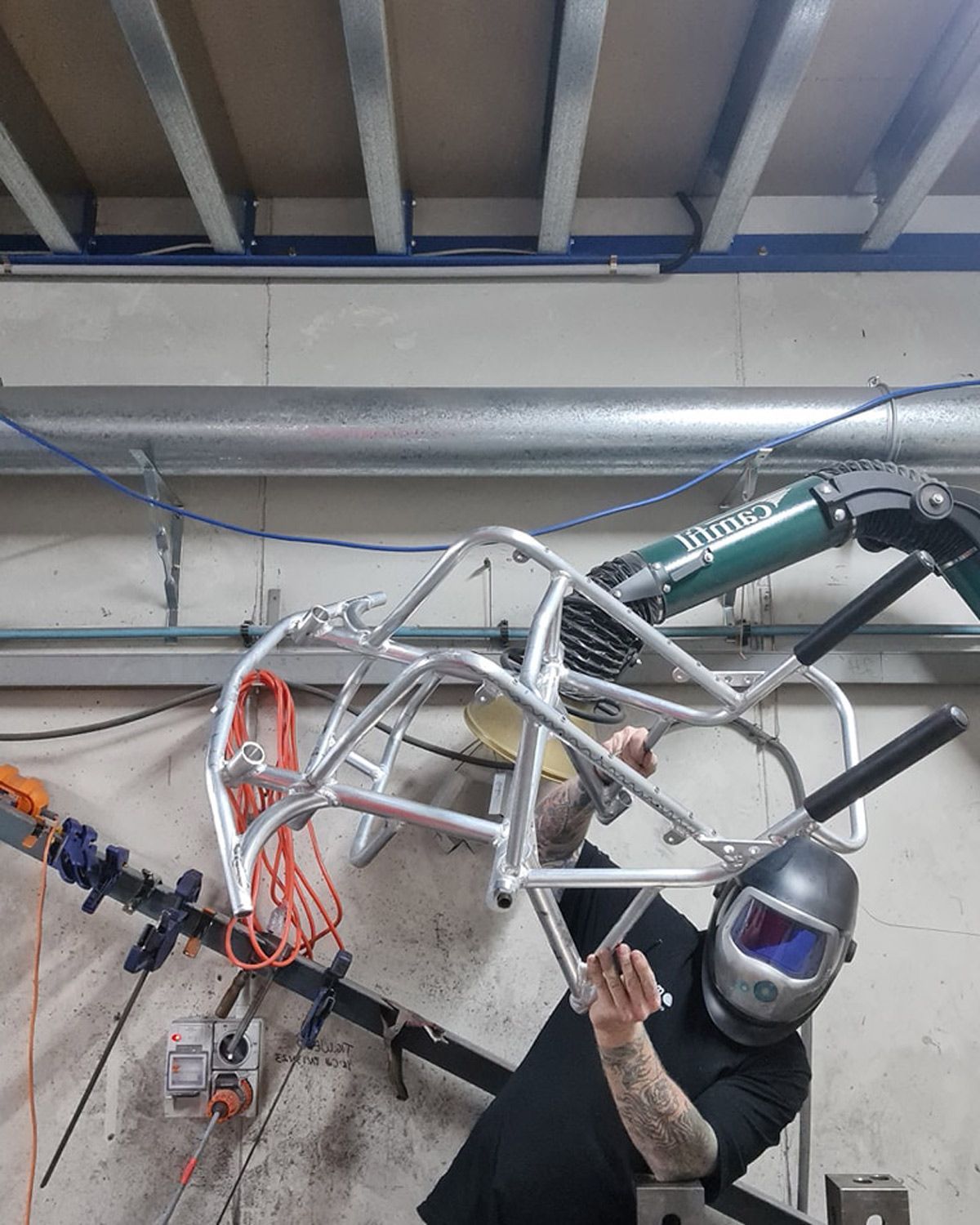 Welder in mask working on a metal frame; workshop setting.