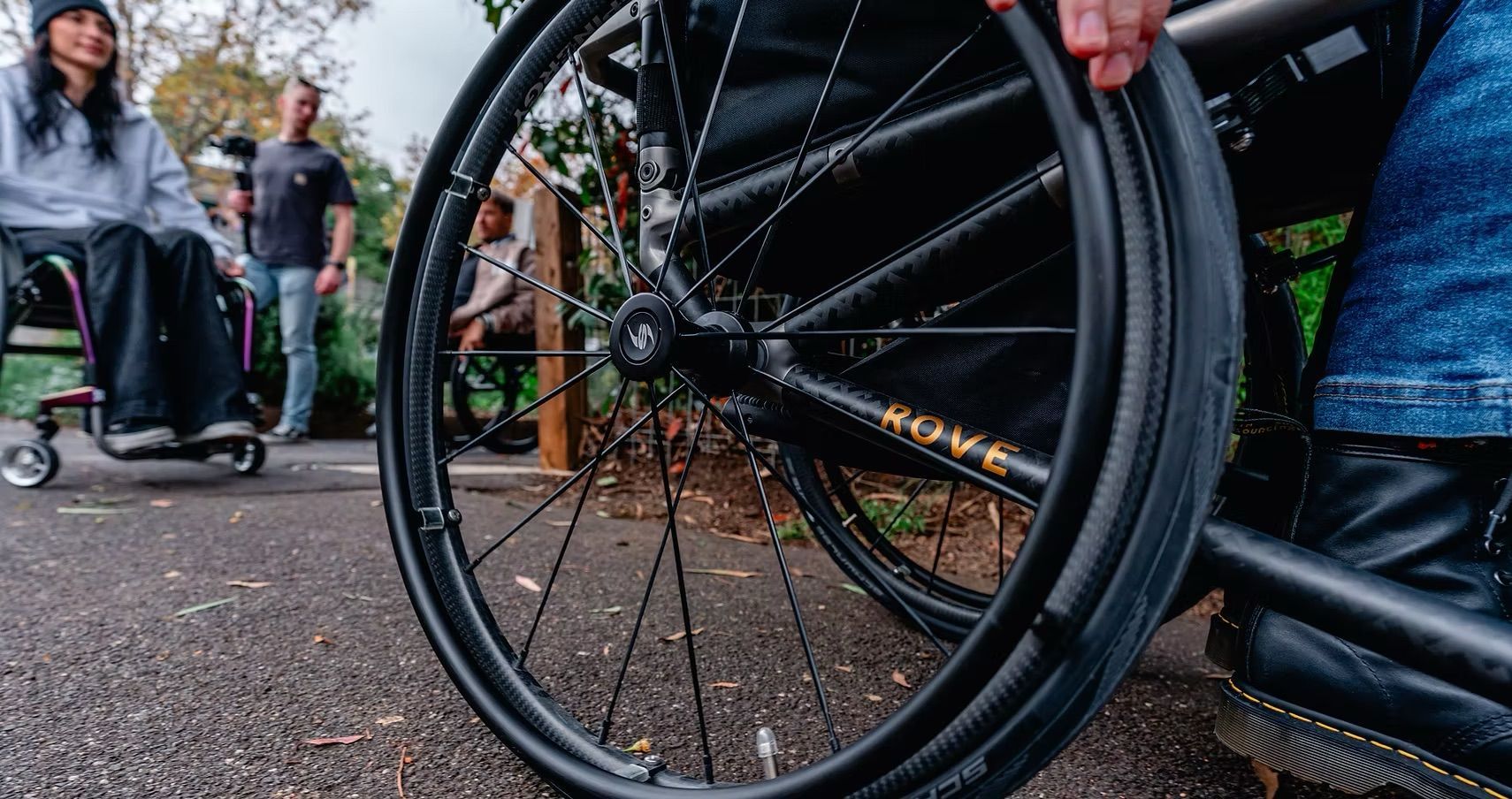 Wheelchair with a black seat and a black storage bag. The wheels are silver with green accents.