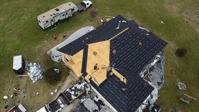 Aerial view of a house with roof damage and debris scattered around it, with a truck nearby