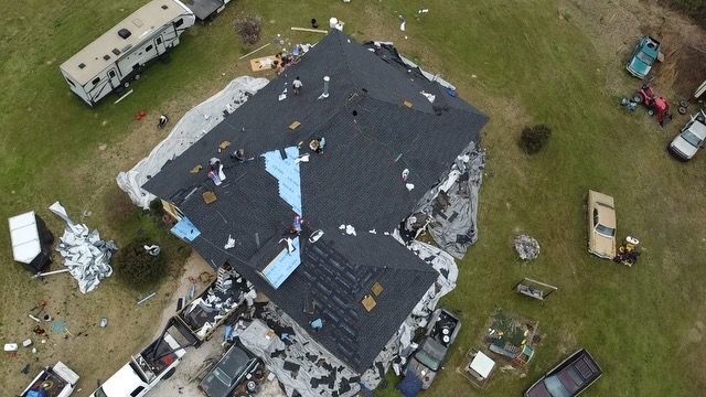 Aerial view of a damaged house with a torn roof and debris scattered across the yard.