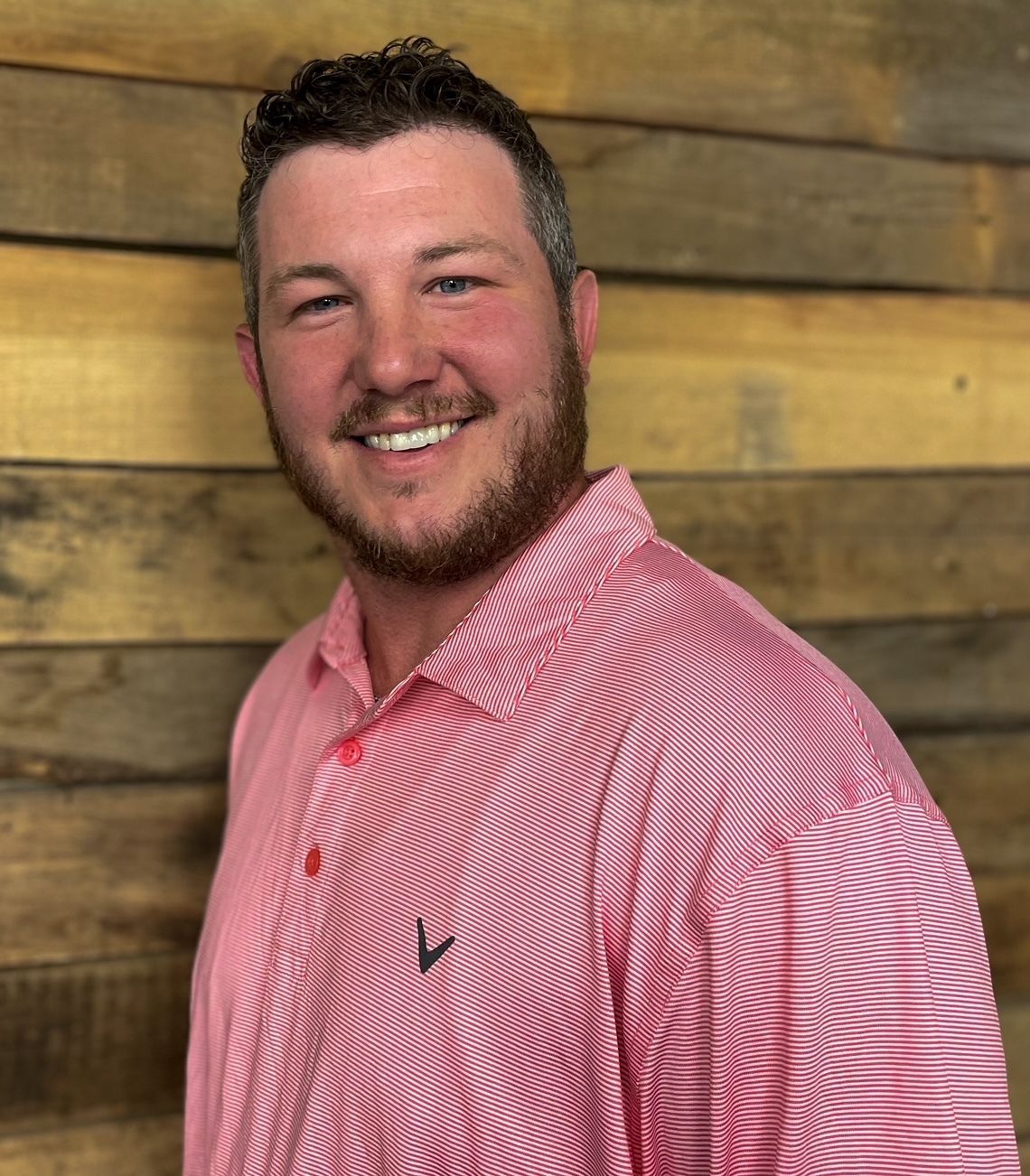 Smiling person in a red striped shirt standing against a wooden wall