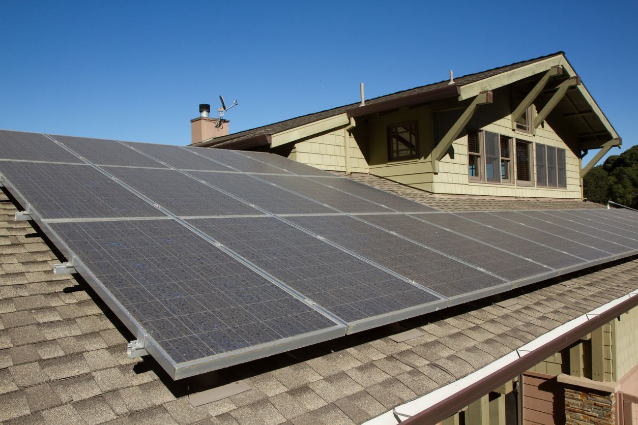 Solar panels on a sloped rooftop in front of a house under a clear sky.