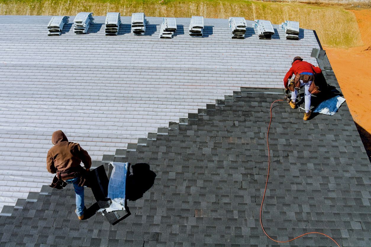 Workers installing shingles on a rooftop, with dark gray and white sections visible.