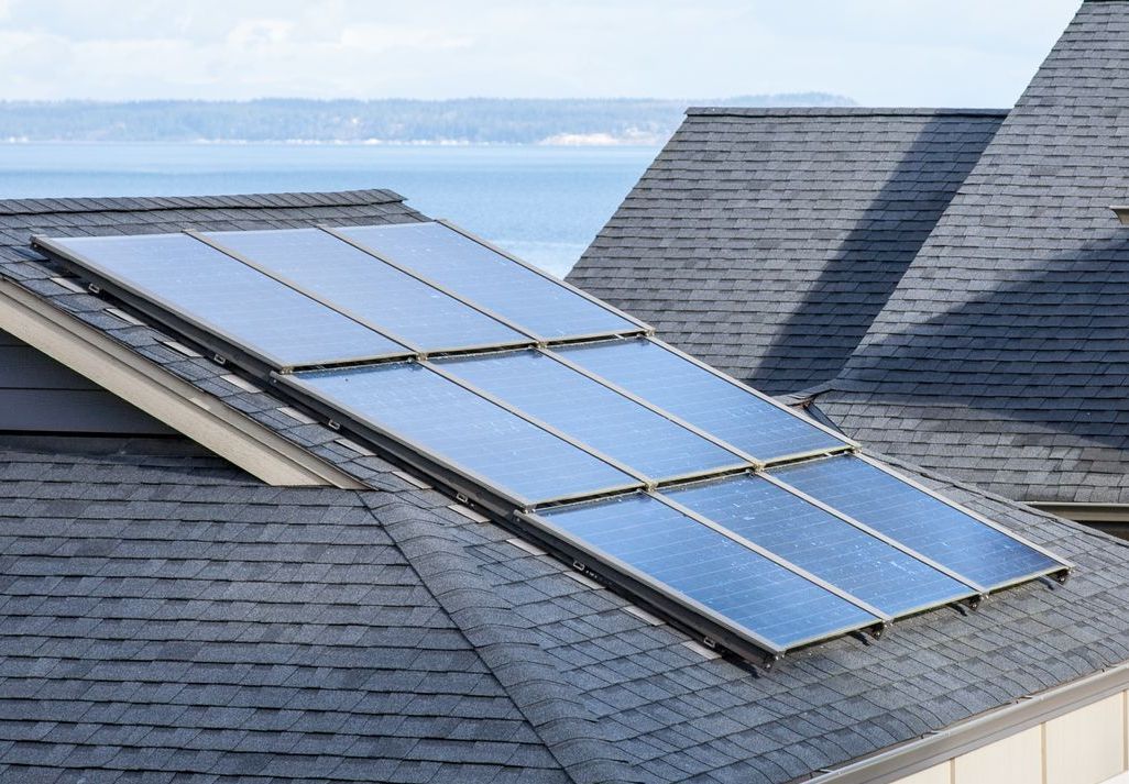 Solar panels mounted on a gray shingled roof near the water