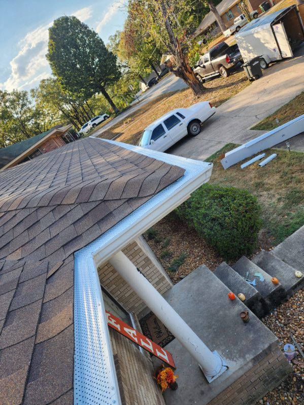Tilted view from a roof over a suburban driveway with a white car, tree, truck, and construction materials below.