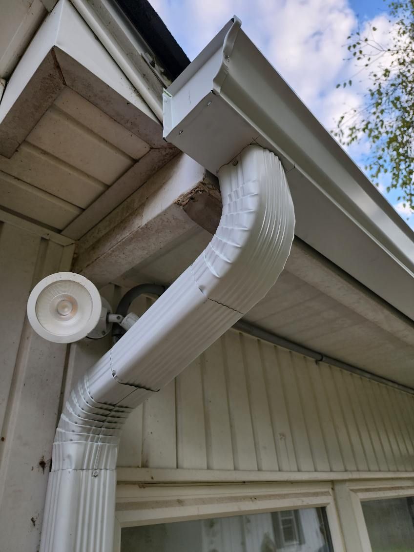 White gutter downspout with flexible extension attached to a house under the eaves