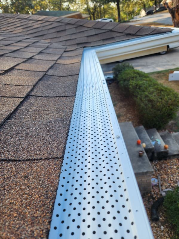 Perforated metal gutter guard along a roof edge above a landscaped yard