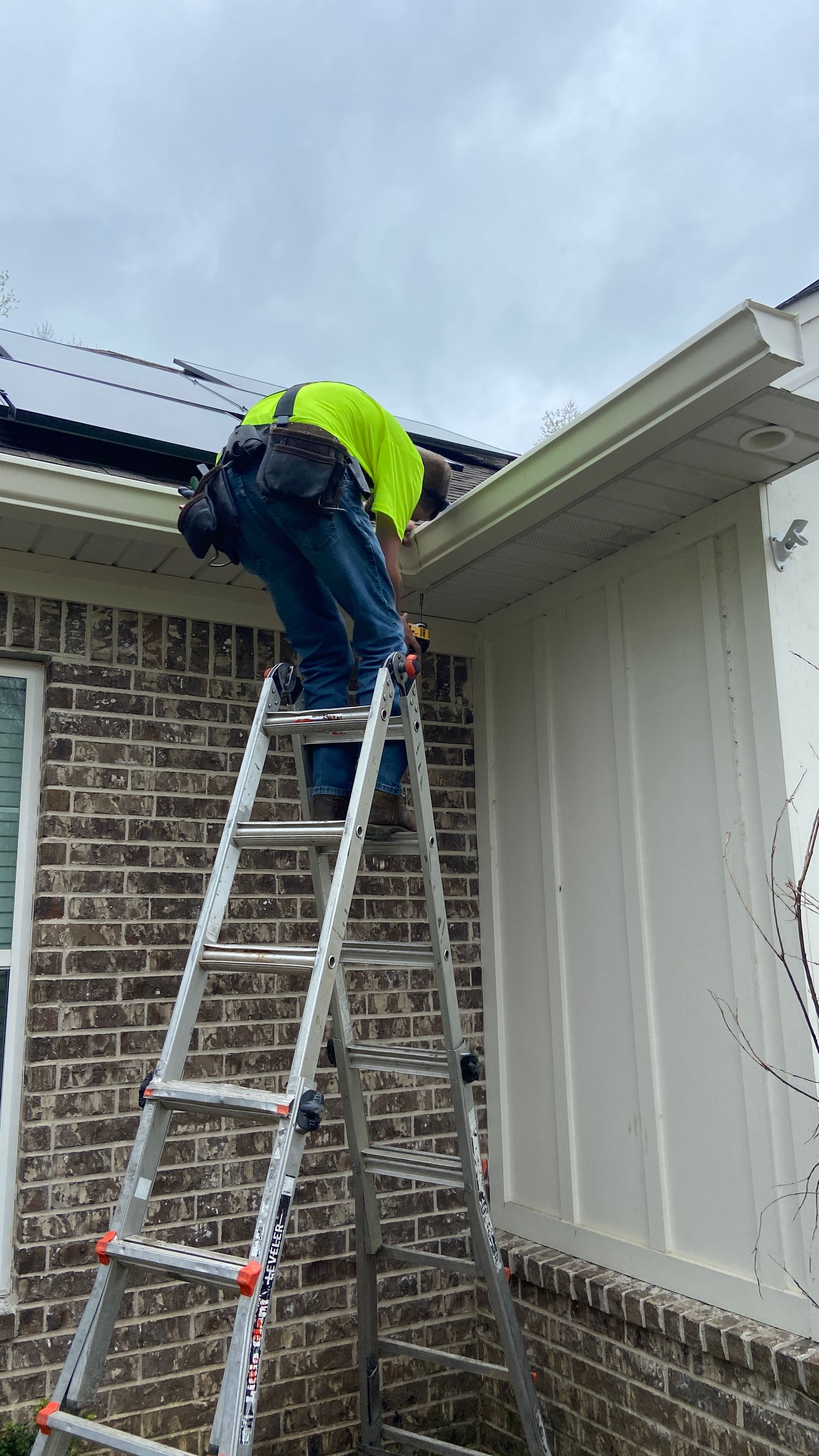 Worker on a ladder repairing a roof gutter on a brick house.