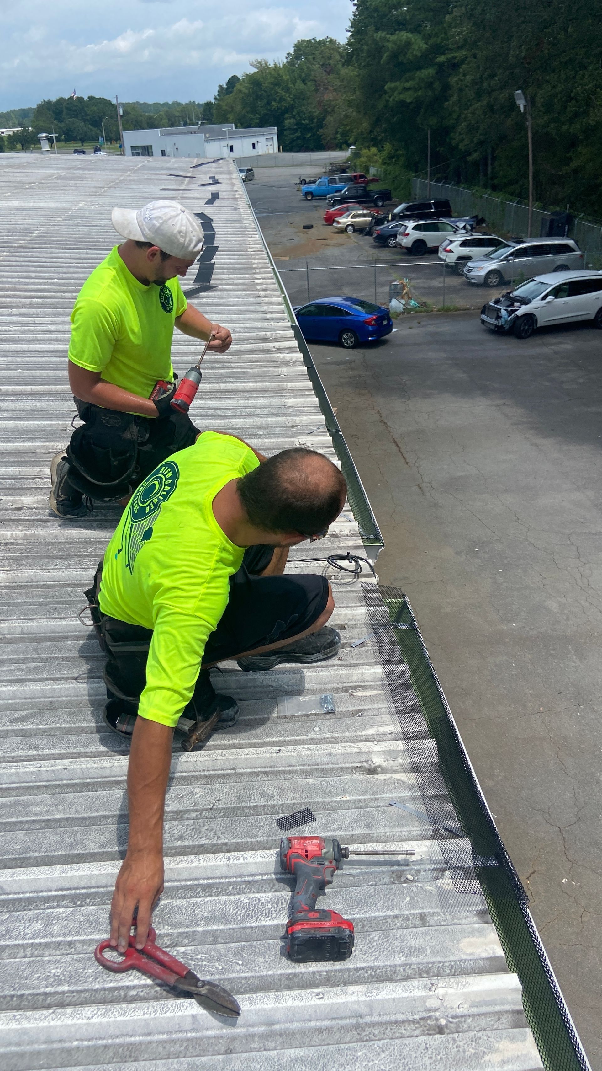 Workers in neon shirts repair a white roof edge overlooking a parking lot.