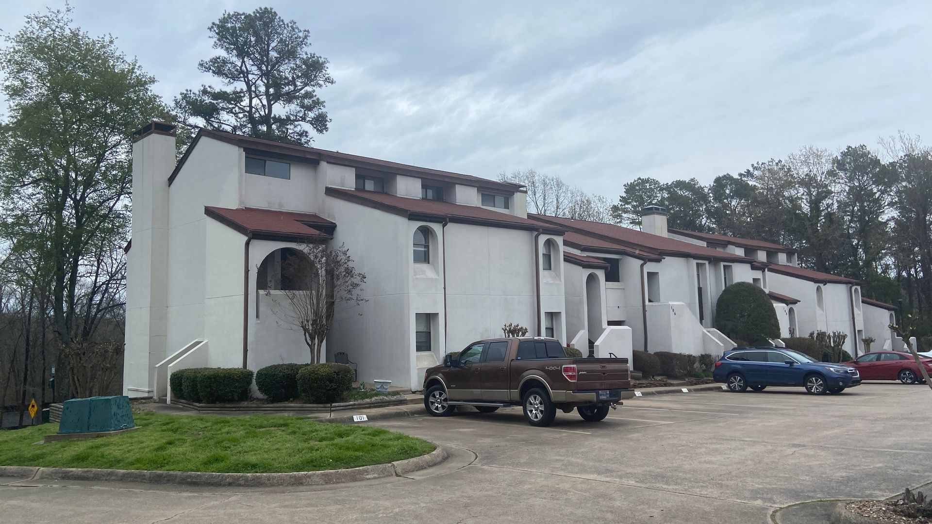 White apartment building with red awnings, parked cars, and trees in front