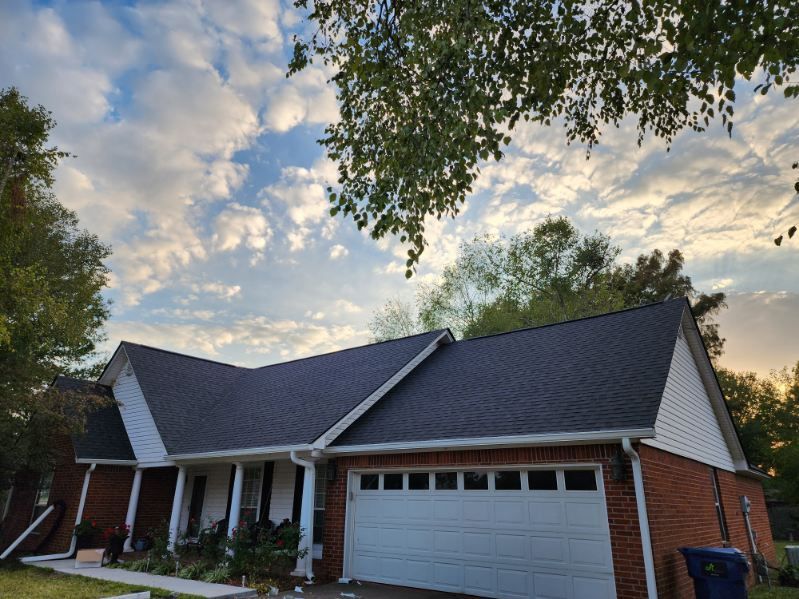 Suburban brick house with dark roof and white garage under a cloudy sunset sky