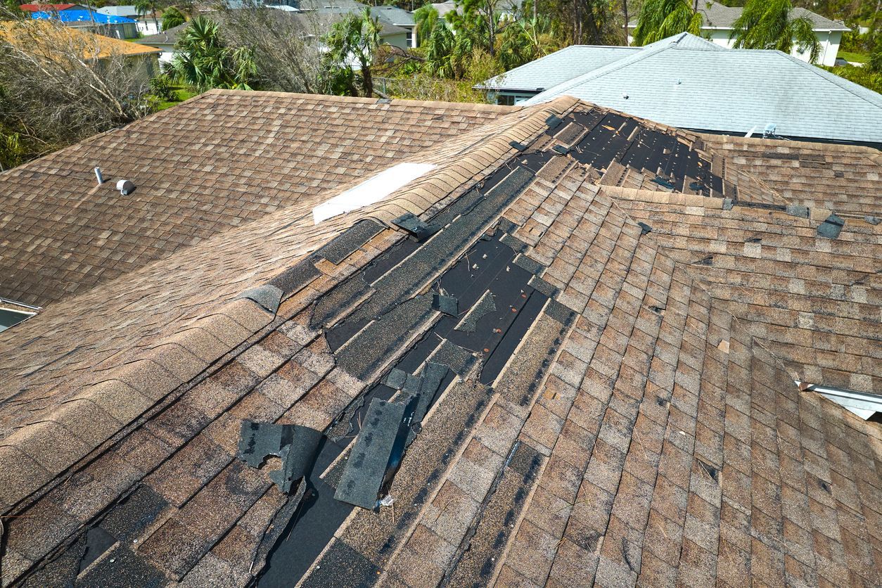 Damaged shingle roof with missing and patched sections next to a corrugated metal roof