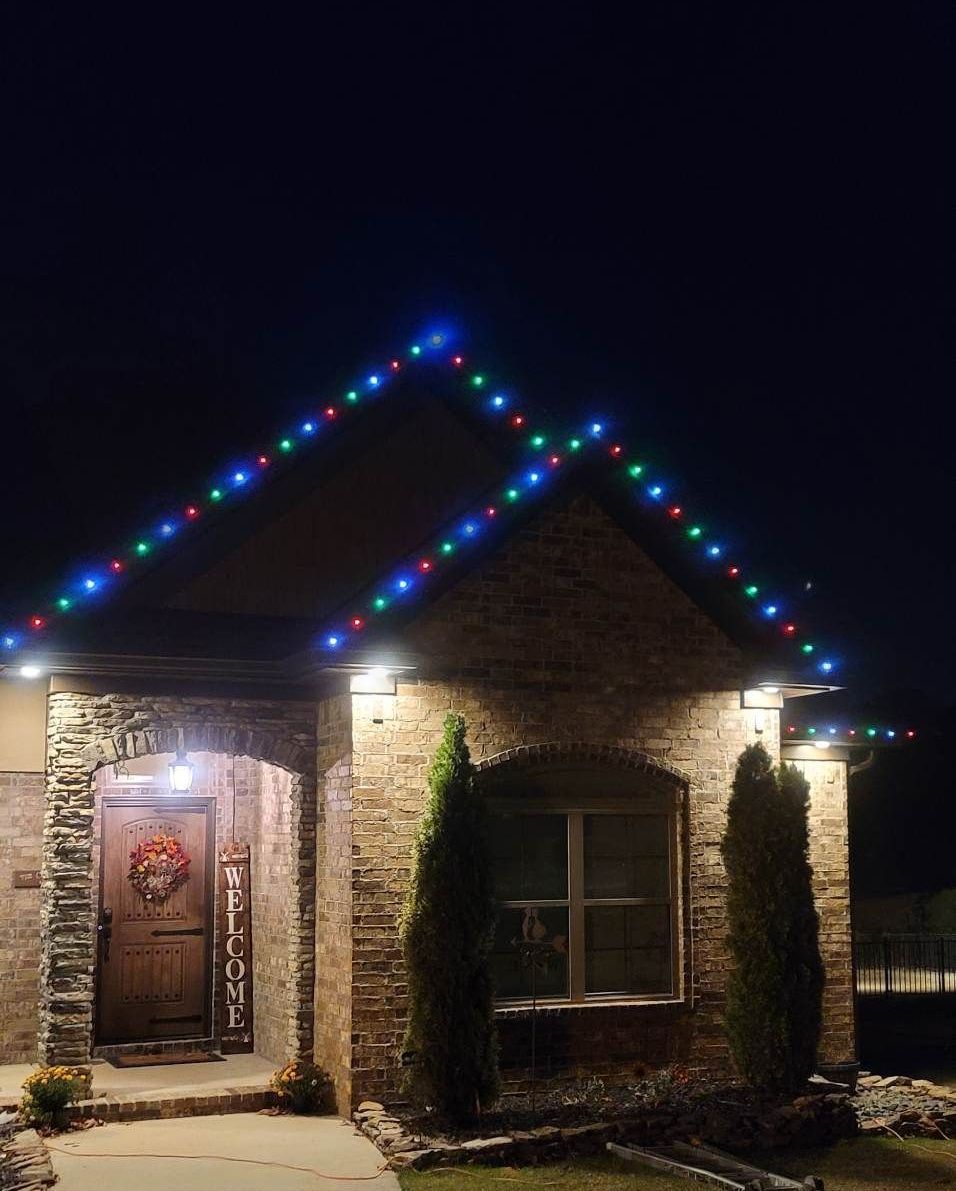 Small stone house at night with colorful string lights along the roofline and a lit front door.