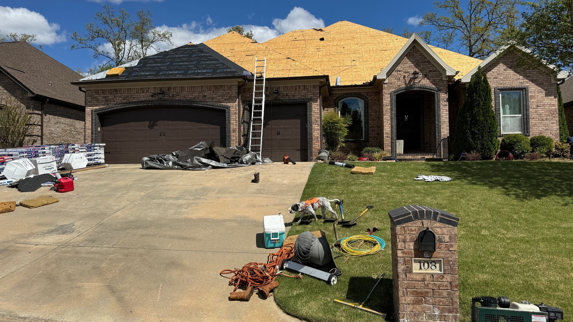 Damaged suburban house with exposed roof, debris in driveway and yard, and moving boxes scattered outside
