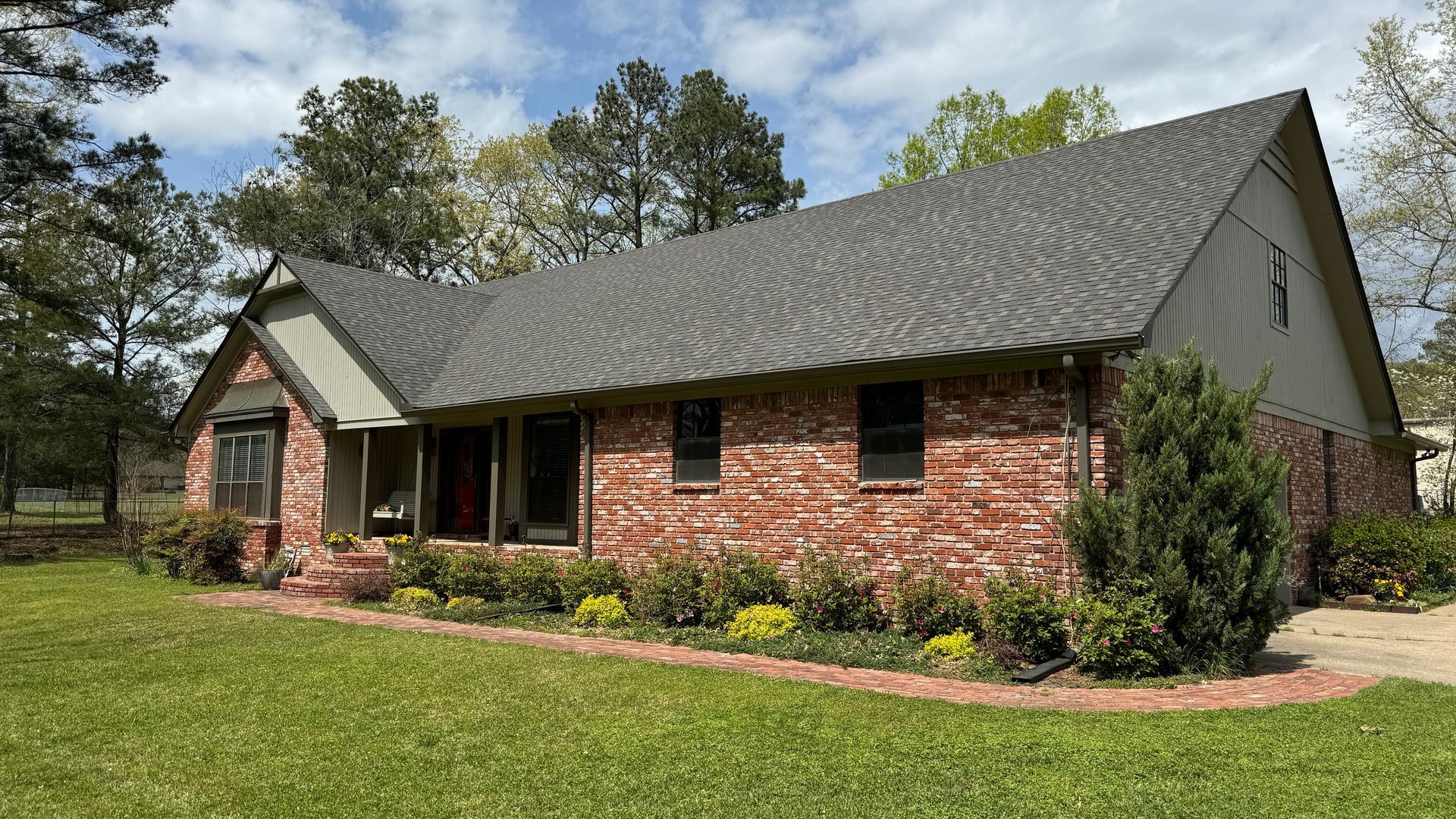 Brick house with dark gray roof, white trim, and a front porch, set on a grassy lawn with trees behind.