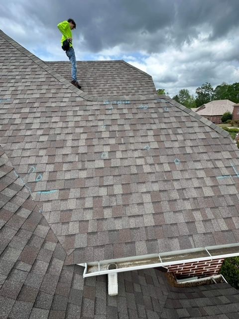 Worker in a neon green jacket on a steep shingled roof during roof repair