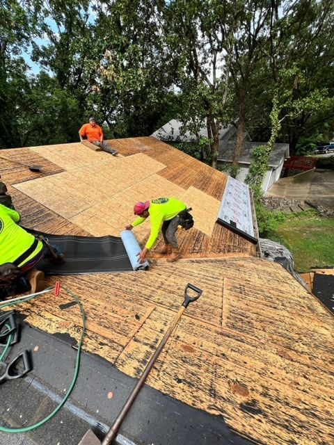 Roofers installing plywood sheathing on a roof, with tools and safety vests visible.