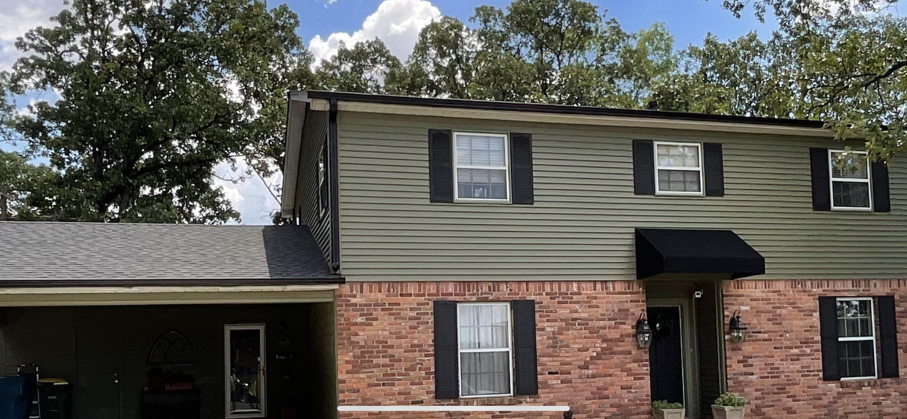 Brick-and-siding two-story house with black shutters and a covered carport under trees