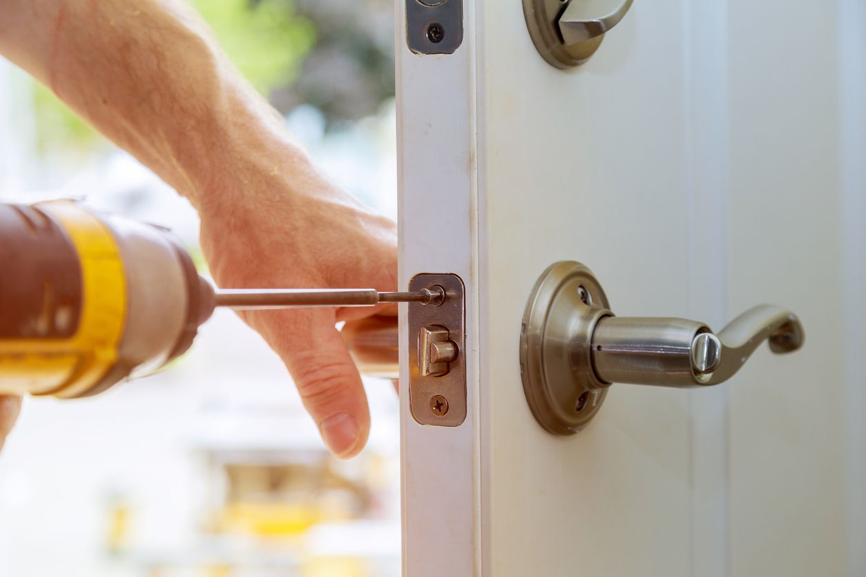 Hand using a screwdriver to adjust a silver door latch beside a modern doorknob
