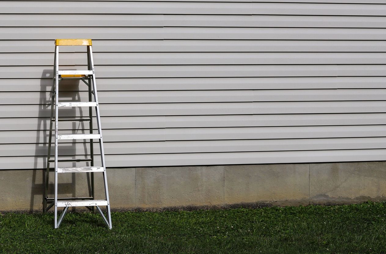 Aluminum ladder leaning against a white garage door above a strip of grass and concrete wall