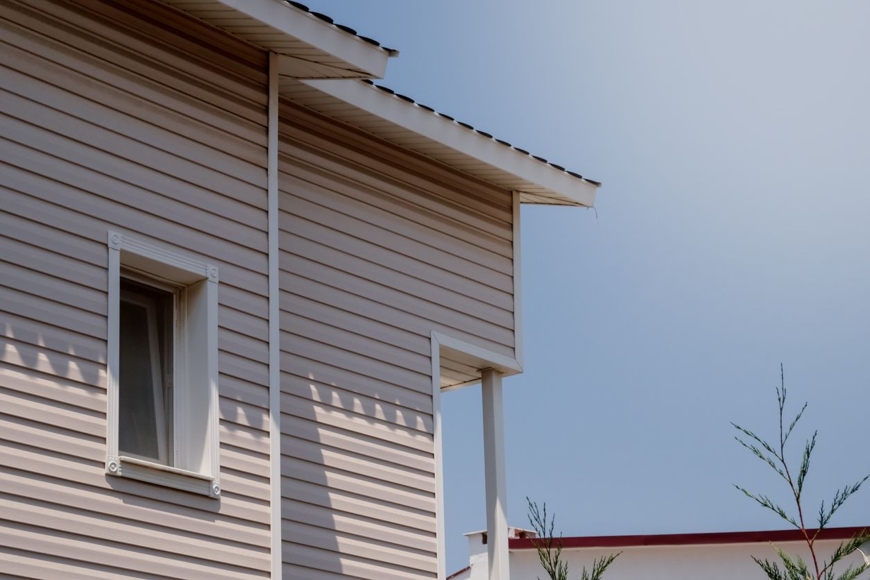 Close-up of a beige house exterior with white trim against a blue sky