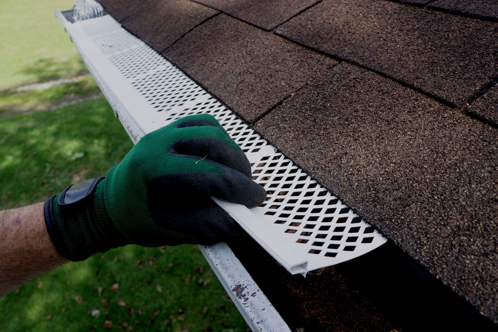Gloved hand installing white perforated roof edge flashing on brown shingle roof
