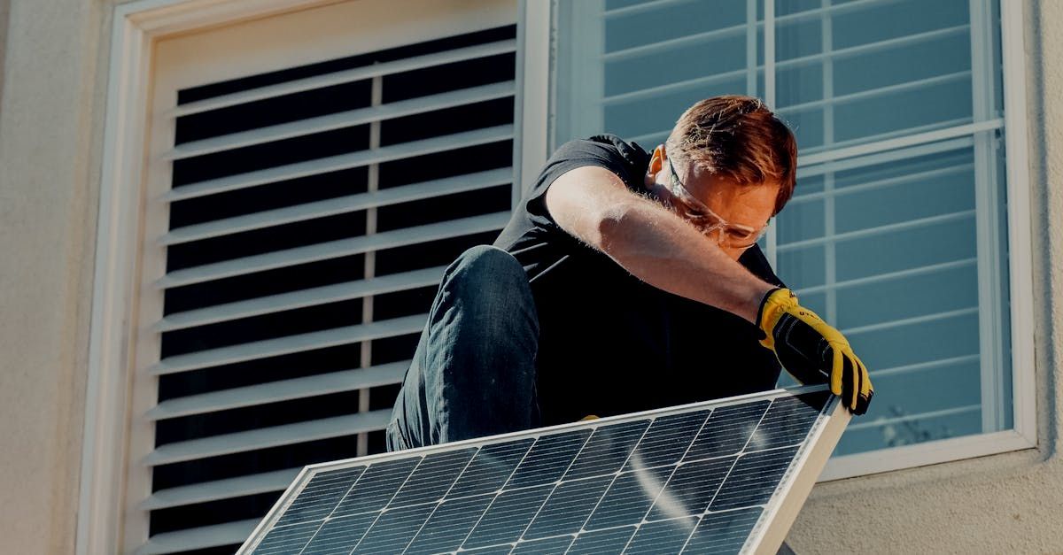 Man installing a solar panel on a house roof, wearing gloves near a window