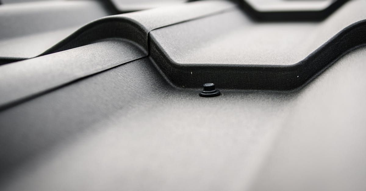 Close-up of black curved roof tiles with a small water droplet on a gray surface