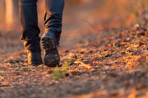 Booted feet walking on a leaf-covered forest path in warm autumn light