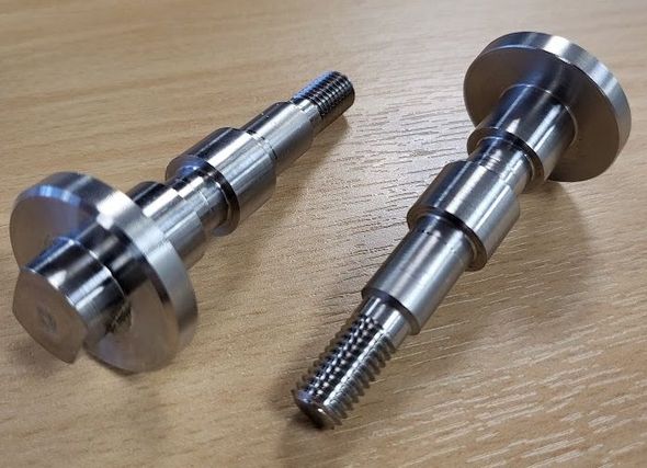 Two metal screws are sitting on a wooden table.