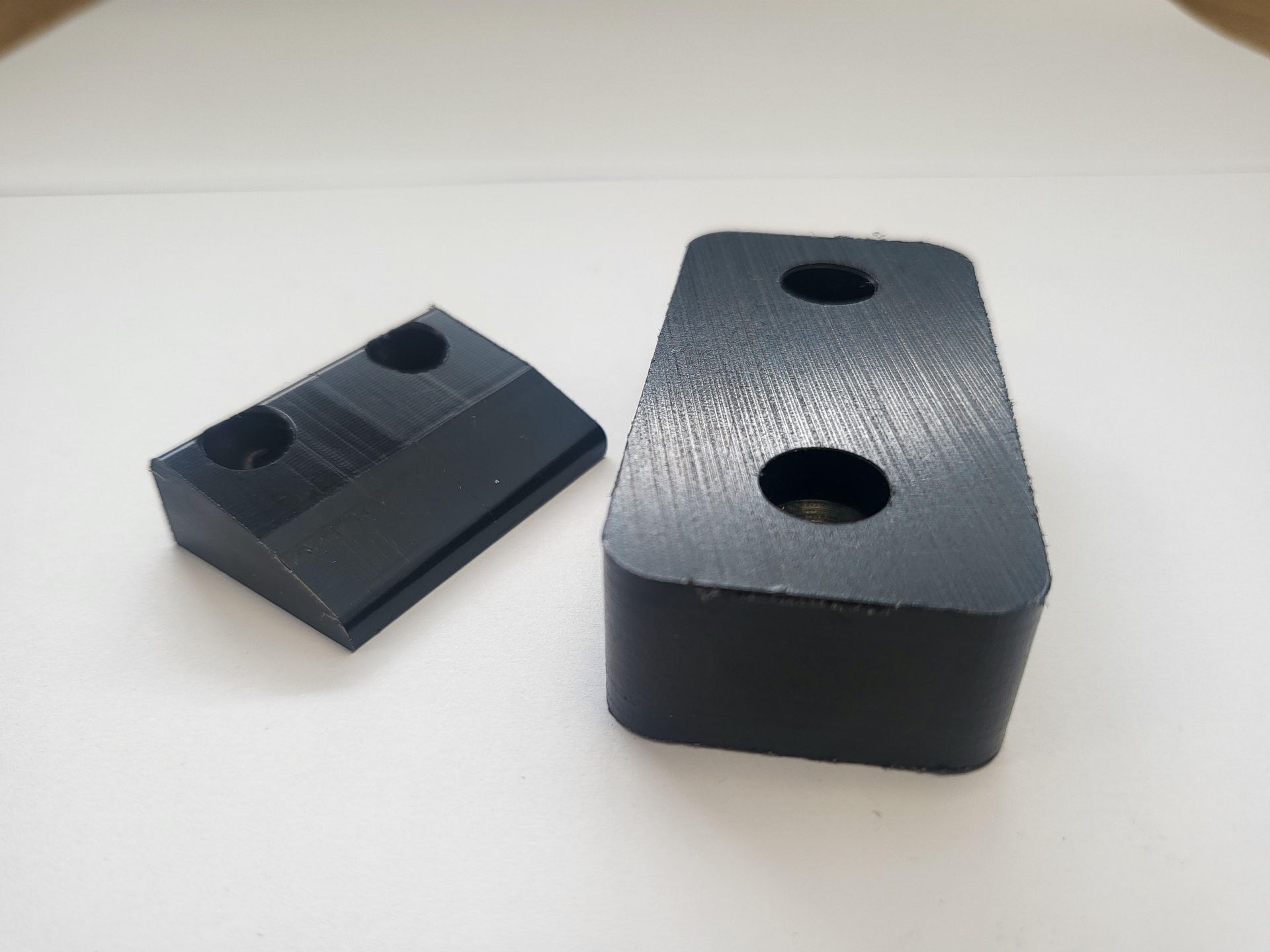 Two black plastic blocks with holes in them on a white surface