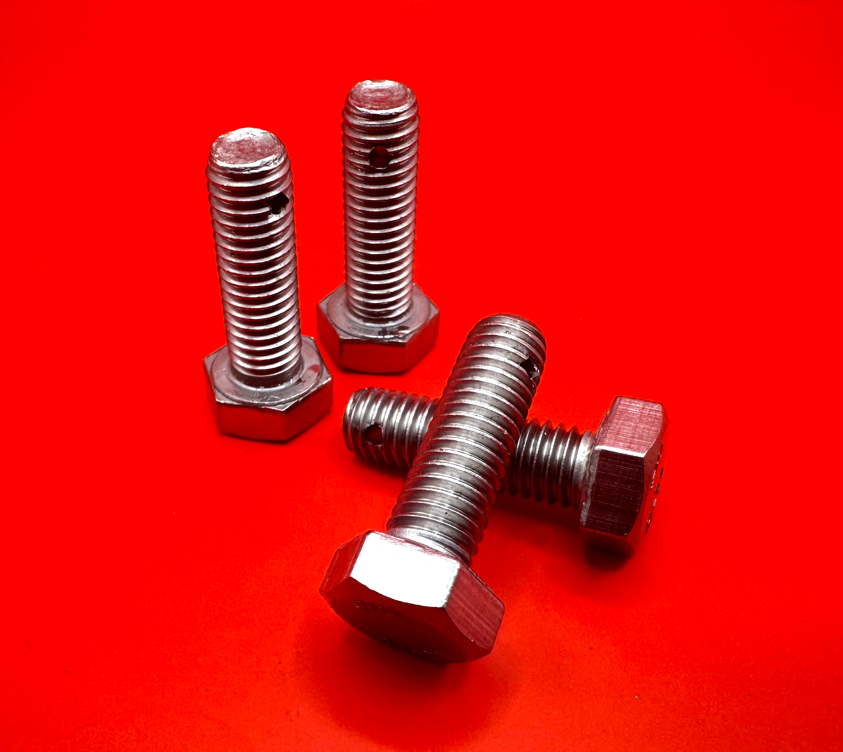 Four silver bolts on a bright red background, one lying diagonally in front.