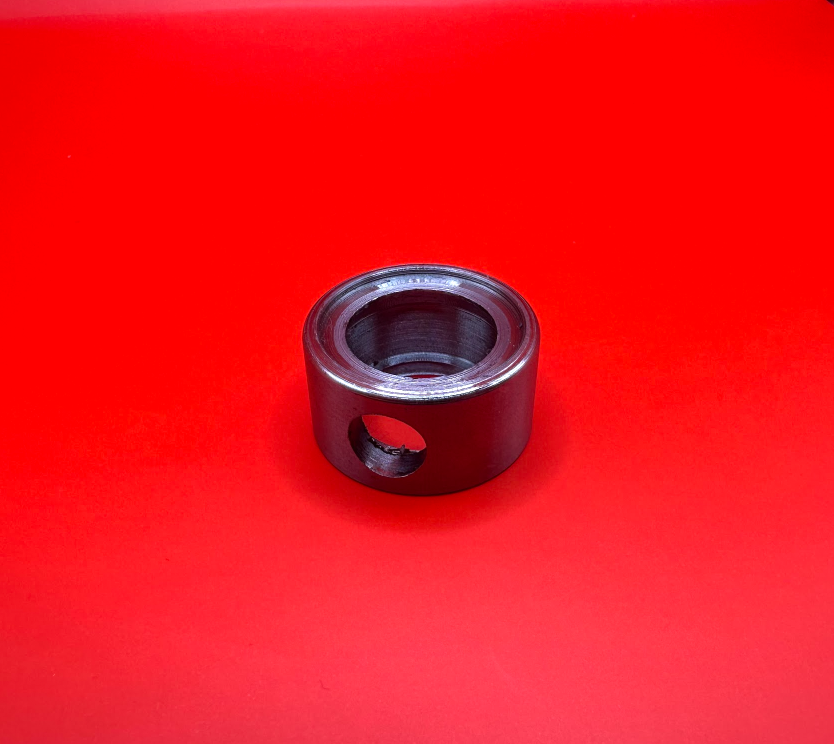 Small dark metal cylindrical part with a side hole on a bright red background