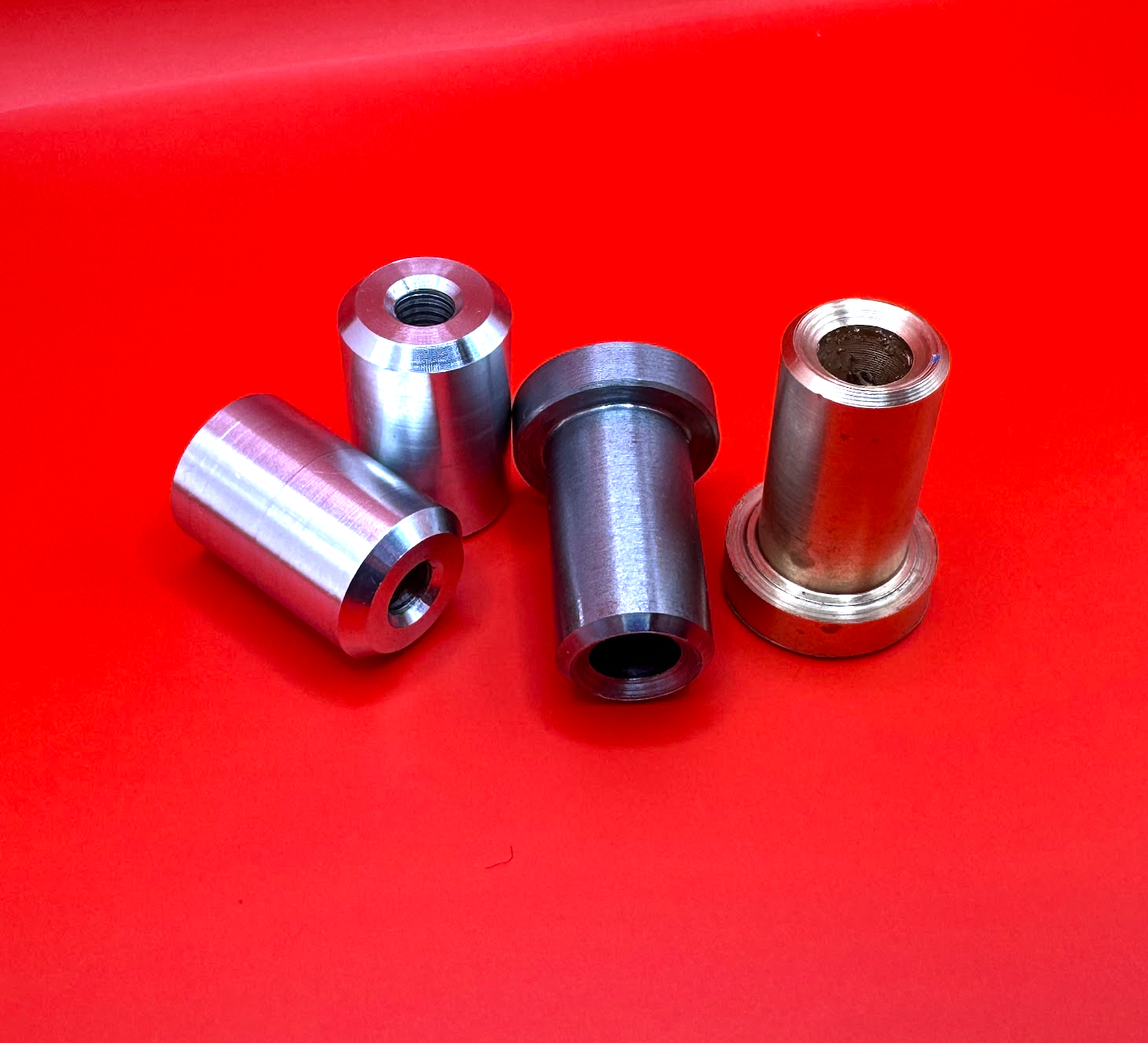 Four small metal machined parts on a bright red surface.