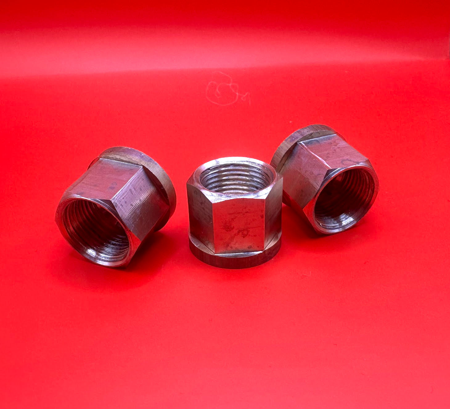 Three metal pipe fittings on a bright red background, with a hex nut centered between two angled fittings