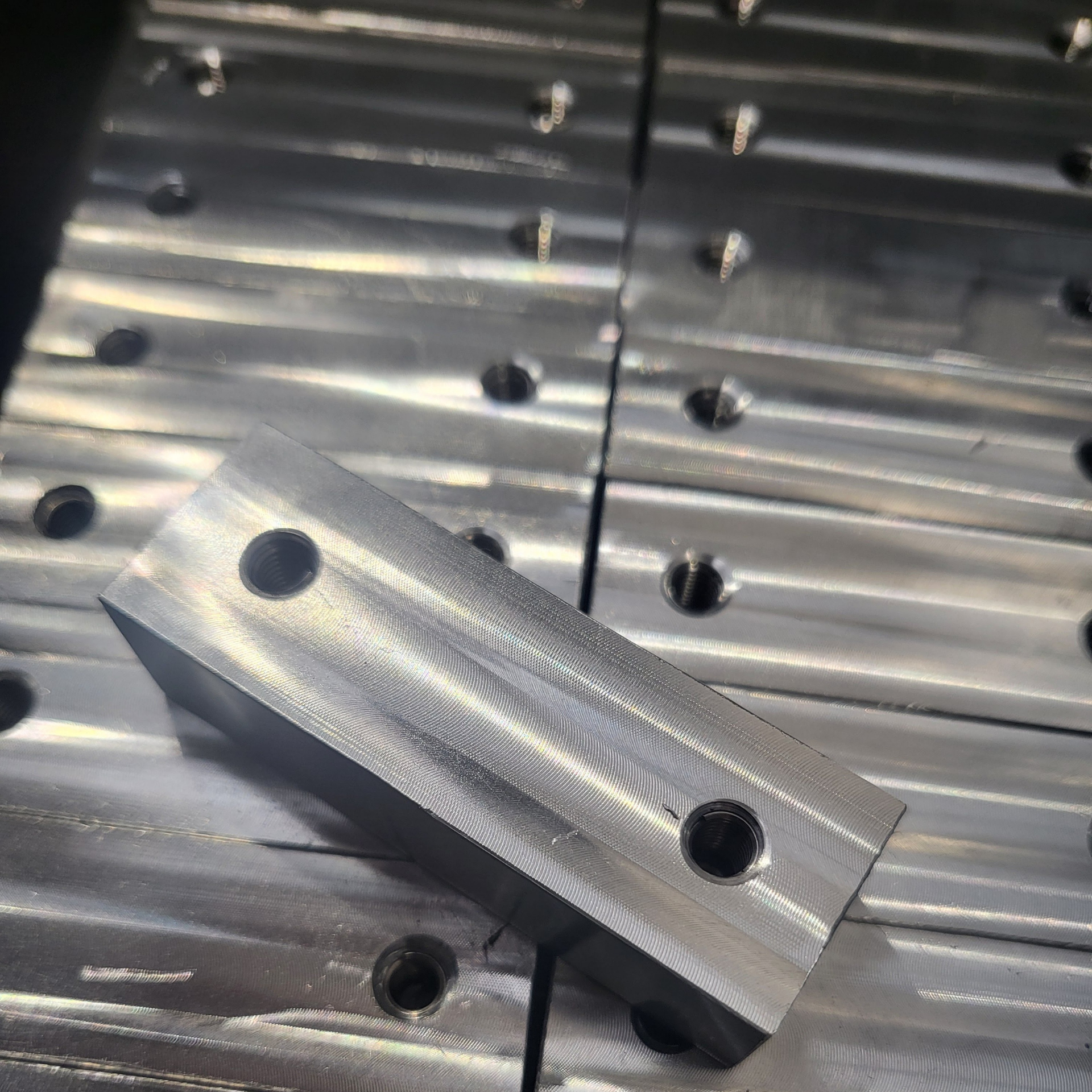 Machined metal blocks with two holes and angled sides, stacked on a metal surface.