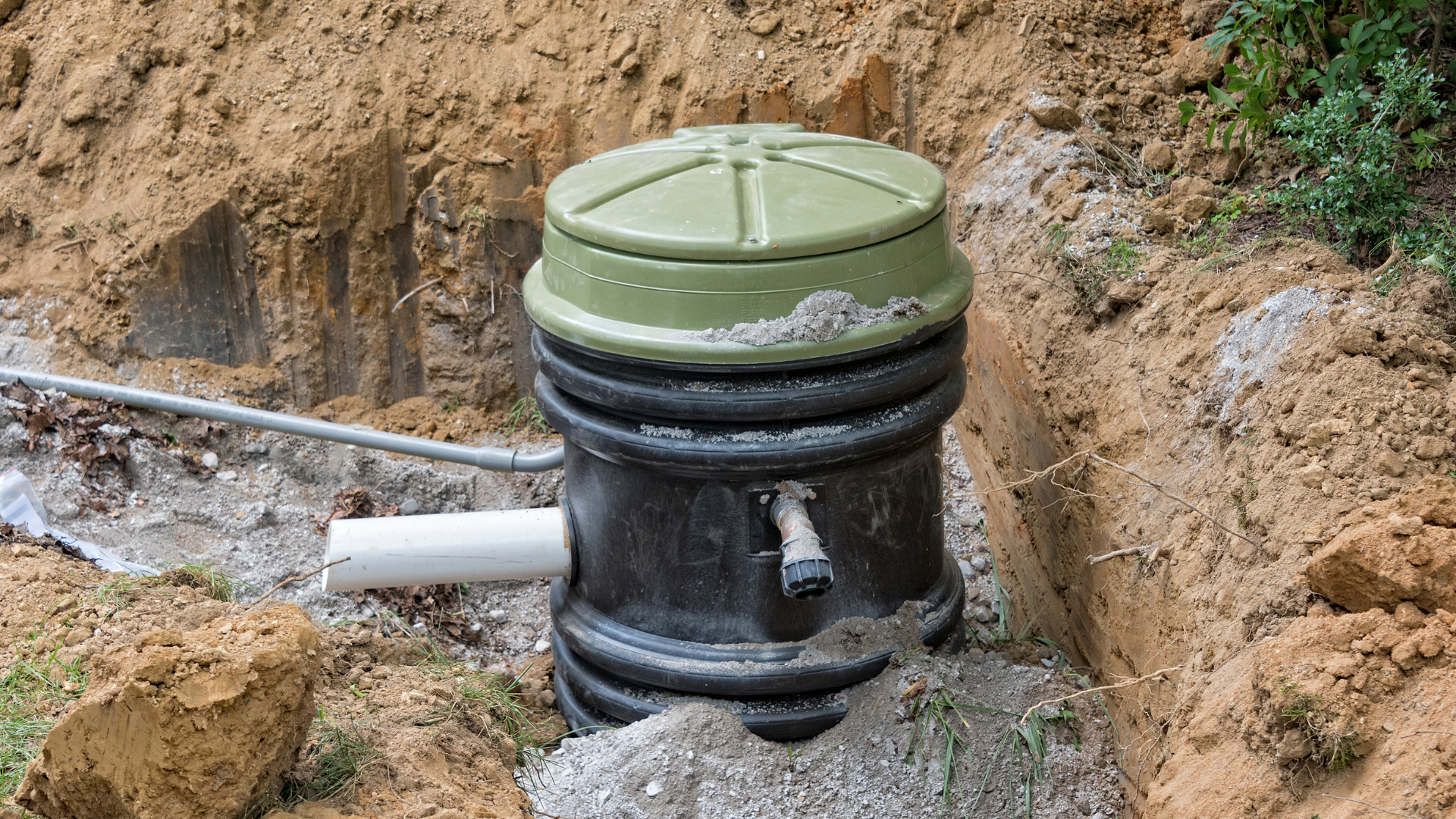 An open pit with a black and green septic tank and a white pipe partially buried.