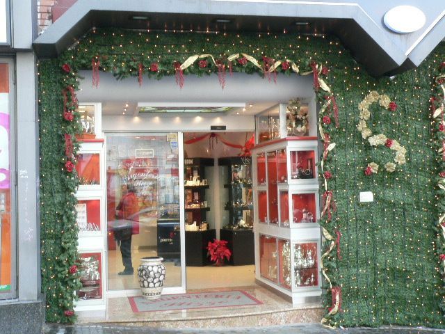 Ingresso del negozio decorato con porte aperte, dettagli rossi e luci natalizie su una parete verde