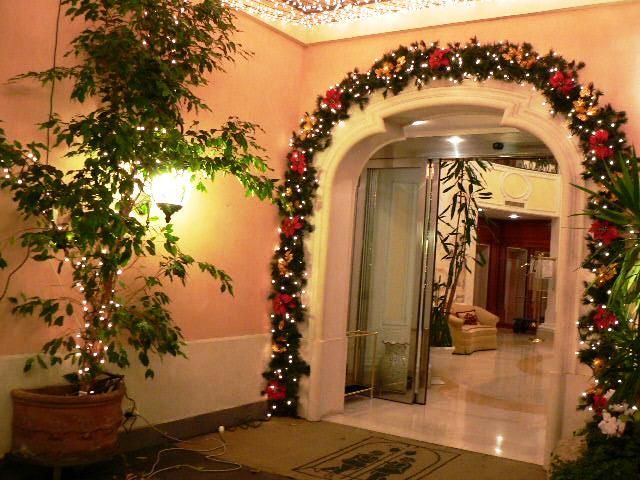 Arco decorato per le feste con luci e ghirlande in un corridoio interno illuminato da una luce calda.