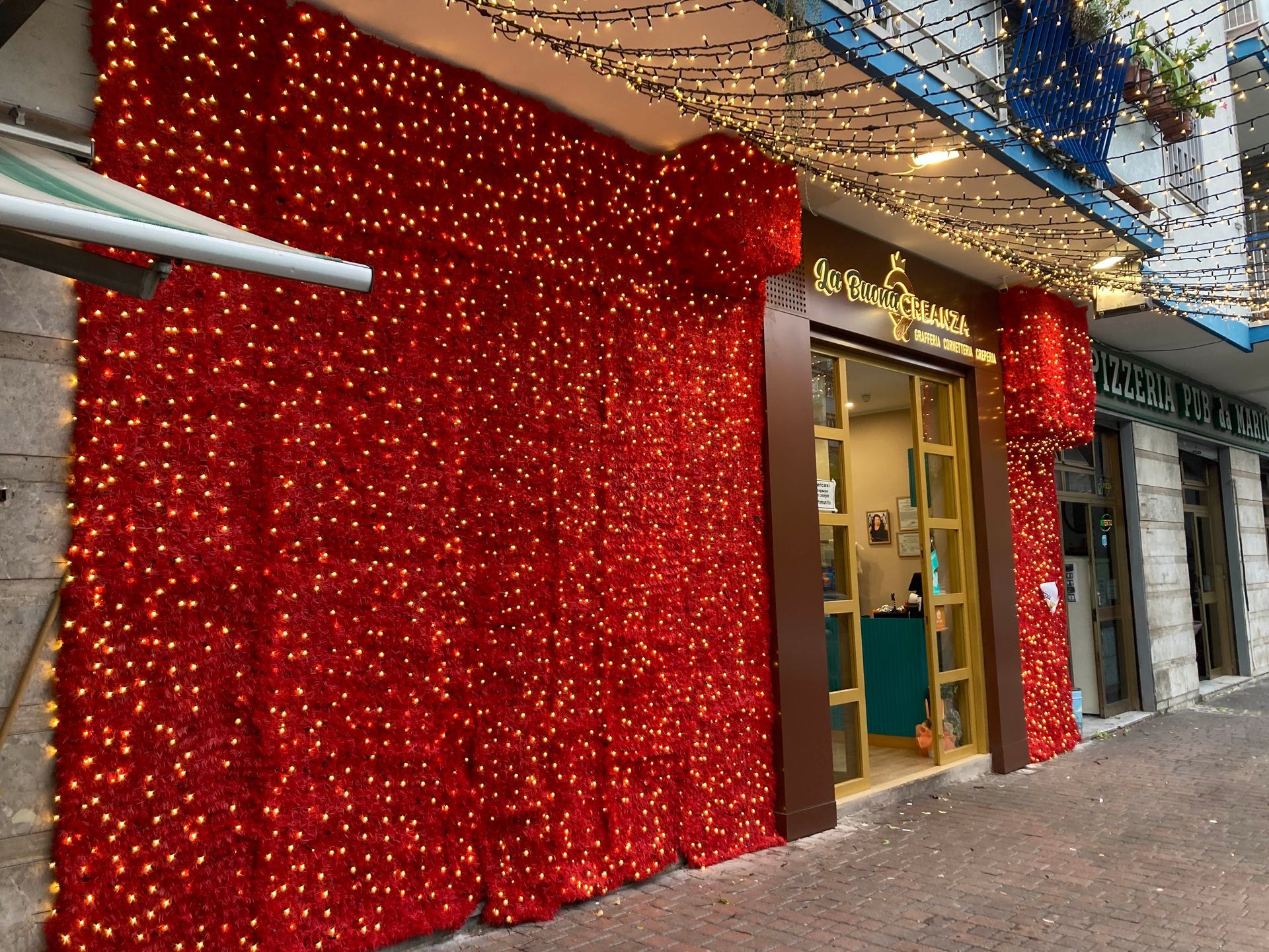 Una vetrina illuminata di rosso, decorata con scintillanti tende rosse e luci natalizie lungo un marciapiede.